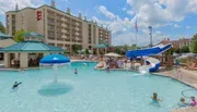 The image shows a lively hotel pool area with guests enjoying the water, a waterslide, and poolside amenities, under a clear sky.