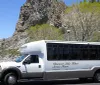A tour bus with Discover Lake Tahoe Scenic Tours printed on its side is parked near a lakeshore with a rocky outcrop in the background under a clear blue sky