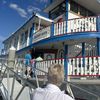 Passengers are boarding a blue and white riverboat called the Barefoot Queen on a sunny day.