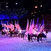 A group of riders on horseback carry the United States flag in an indoor equestrian show, creating a vibrant and patriotic display.