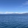 The image shows a serene blue lake with a mountain range in the background under a clear sky with scattered clouds.