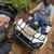 Two people wearing helmets are taking a selfie while riding an all-terrain vehicle (ATV) on a muddy trail.