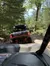 The image shows a view from inside an off-road vehicle following another off-roader through a forest trail.
