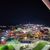 The image captures a bustling amusement park with go-kart tracks and colorful lighting at nighttime, viewed from an elevated perspective.