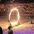 The image captures a performer on horseback jumping through a large ring of fire in front of an audience.