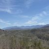 The image shows a scenic view of a mountain range with a clear blue sky and sparsely distributed houses nestled among leafless trees.