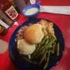 The image shows a hearty meal consisting of shredded meat on a bun, mashed potatoes, green beans, and gravy, served on a blue plate with a bottle of ketchup and a container of dressing on the side, all set on a red table.