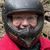 Two people are wearing helmets and sitting on all-terrain vehicles (ATVs) on a dirt trail surrounded by forest.