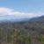 A scenic landscape showcasing lush greenery, rolling hills, and a mountain range under a partly cloudy sky.