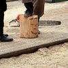 A person stands beside a chainsaw and a wood stump with a carved number 