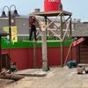 A person is standing on a platform working on a wooden structure with a red water tower labeled 