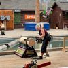 A person is participating in a lumberjack competition, operating a chainsaw to cut through a log in an outdoor setting with a backdrop of target boards and an American flag.