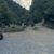 A group of people on all-terrain vehicles are on a gravel road near a forested hillside.