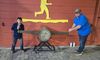 A boy and a man are posing with a large two-handled saw in front of a wooden wall with a yellow lumberjack silhouette at the Lumberjack Feud attraction.