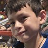 A young boy is smiling at the camera while holding a round piece of wood with the words 