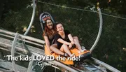 Two people are enjoying a thrilling ride on a mountain coaster, laughing joyfully as they descend the track.