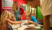 A family is engaged in an interactive exhibit, with adults and children focused on an activity at a table.