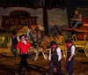 Performers in Wild West attire are present in front of a stagecoach with one man smiling and twirling a lasso evoking the atmosphere of a classic western show