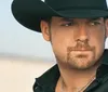 A man wearing a cowboy hat gazes intently at the camera against a blurred natural background