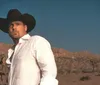 A man wearing a cowboy hat gazes intently at the camera against a blurred natural background