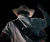 A man wearing a cowboy hat gazes intently at the camera against a blurred natural background