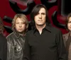 Four male band members are posing in front of a red and black abstract background