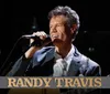 A person is singing into a microphone while playing a guitar with the name Randy Travis displayed at the bottom