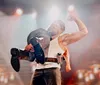 A wrestler is performing a victory pose in the ring showcasing his muscles while holding another wrestler on his shoulder