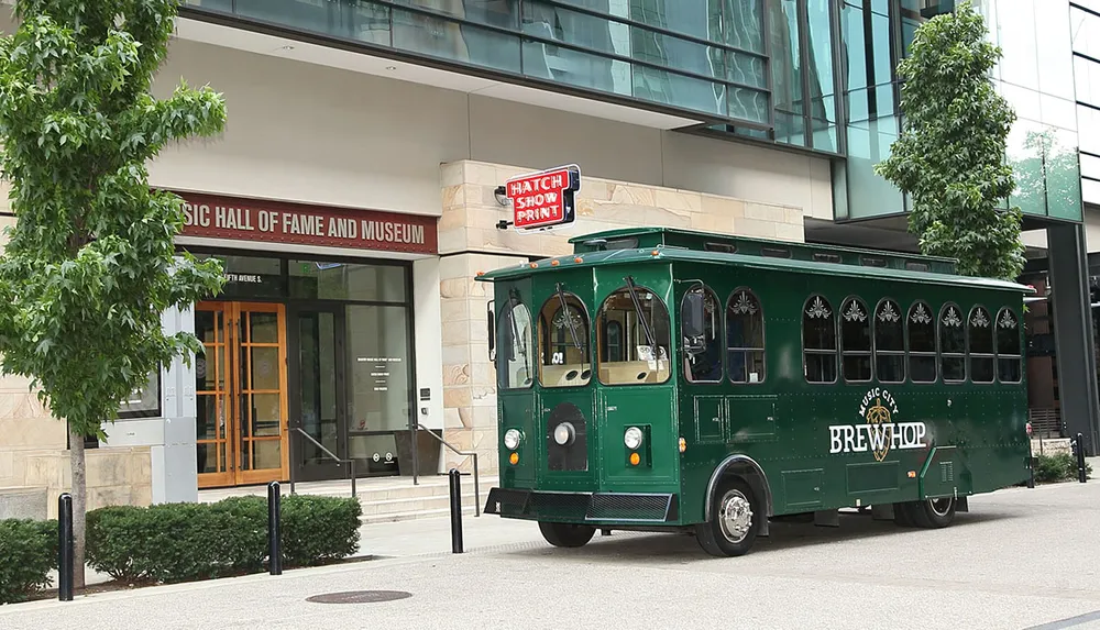 A vintage-style green trolley bus labeled Music City BrewHop is parked in front of a building with a sign that reads Music Hall of Fame and Museum