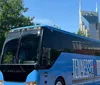 A bus with Tennessee Titans branding is parked on a sunny street with trees and the distinctive ATT Building also known as the Batman Building visible in the background