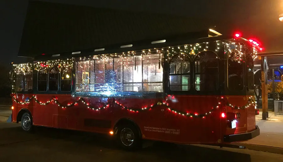 A trolley bus adorned with festive holiday lights is parked in the evening.