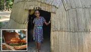 A smiling child is standing in the doorway of a thatch-roofed hut.