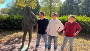 Three men mimic the pose of a statue, standing confidently with hands on hips in a sunny outdoor setting.