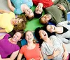 A group of happy people are lying on a colorful floor in a circle with their heads together laughing and smiling