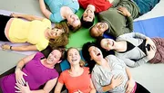 A group of happy people are lying on a colorful floor in a circle with their heads together, laughing and smiling.