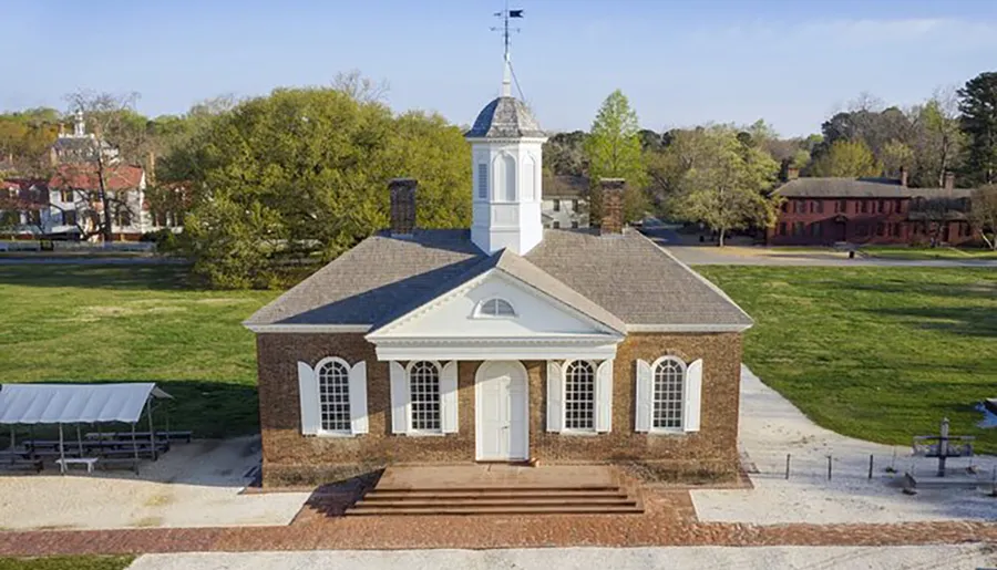 An aerial view of a colonial style brick courthouse with a white cupola, situated in a grassy area with surrounding historic buildings.