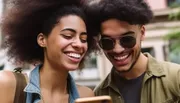 Two happy young people are looking at a smartphone screen together on a sunny day.