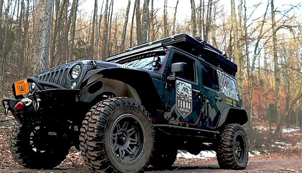 A modified off-road vehicle is parked in a wooded area with custom graphics and equipment for rugged terrain