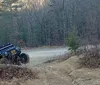 A rugged off-road vehicle equipped with roof-mounted gear is parked in a woodland area near a simple wooden structure with a solar panel on its roof