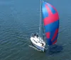 A sailboat with its sails unfurled glides through the water with a couple of people aboard