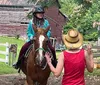 Two people are riding horses near a barn in a rural setting