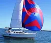 A sailboat with a red and blue spinnaker sails on a clear day with people visible on deck