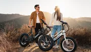 A man and a woman are standing with electric bicycles outdoors, enjoying a sunny day.