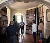 A group of people is on a tour in an elegant room with arched doorways and wall-to-ceiling bookshelves filled with old books