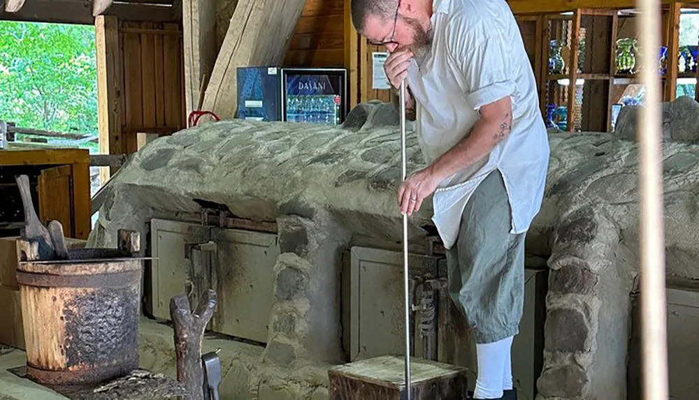 A person is working with glass using tools near a large furnace in a glassblowing workshop