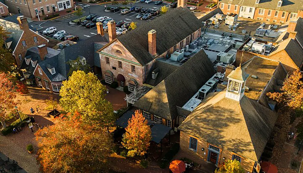 An aerial view of a quaint brick-built historic district with autumn-colored trees and a parking area bathed in soft sunlight