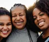 Three smiling women with curly hair are posing closely together likely indicating a familial or close relationship