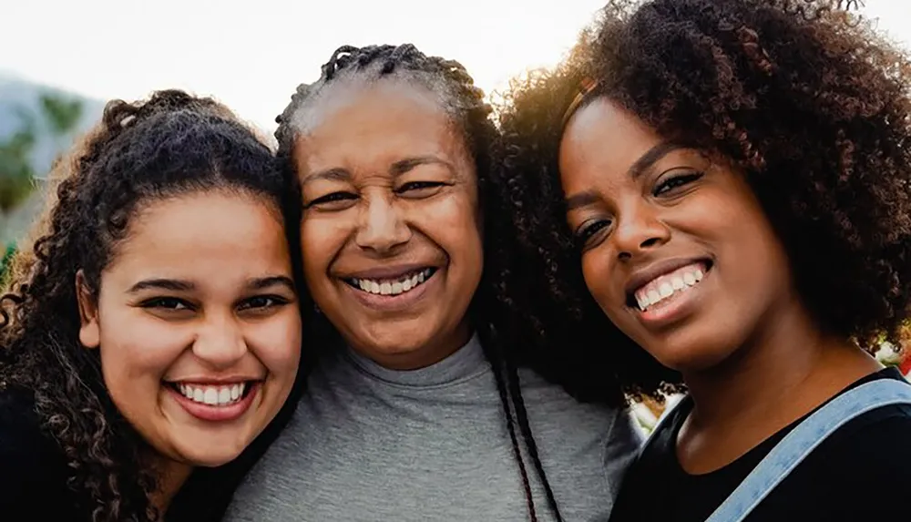 Three smiling women with curly hair are posing closely together likely indicating a familial or close relationship