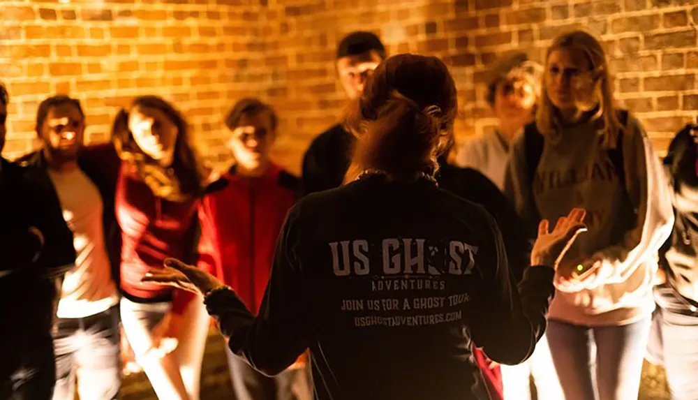 A group of people are attentively participating in an evening ghost tour led by a guide wearing a jacket that reads US GHOST ADVENTURES