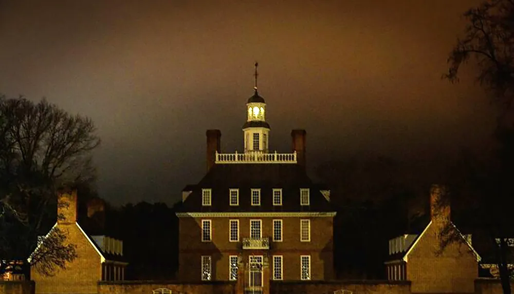 The image shows a large historic brick building illuminated at night with the central section topped by a glowing cupola